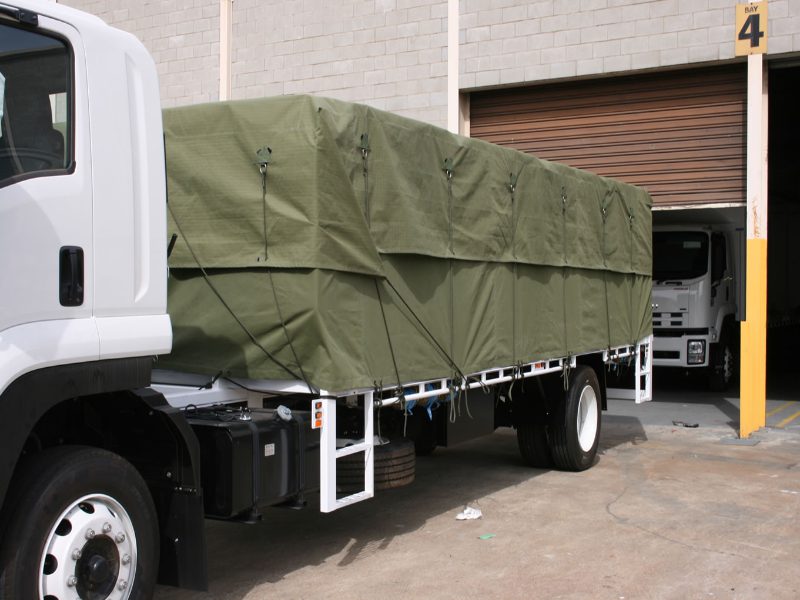 Truck with green tarpaulin parked outside warehouse.