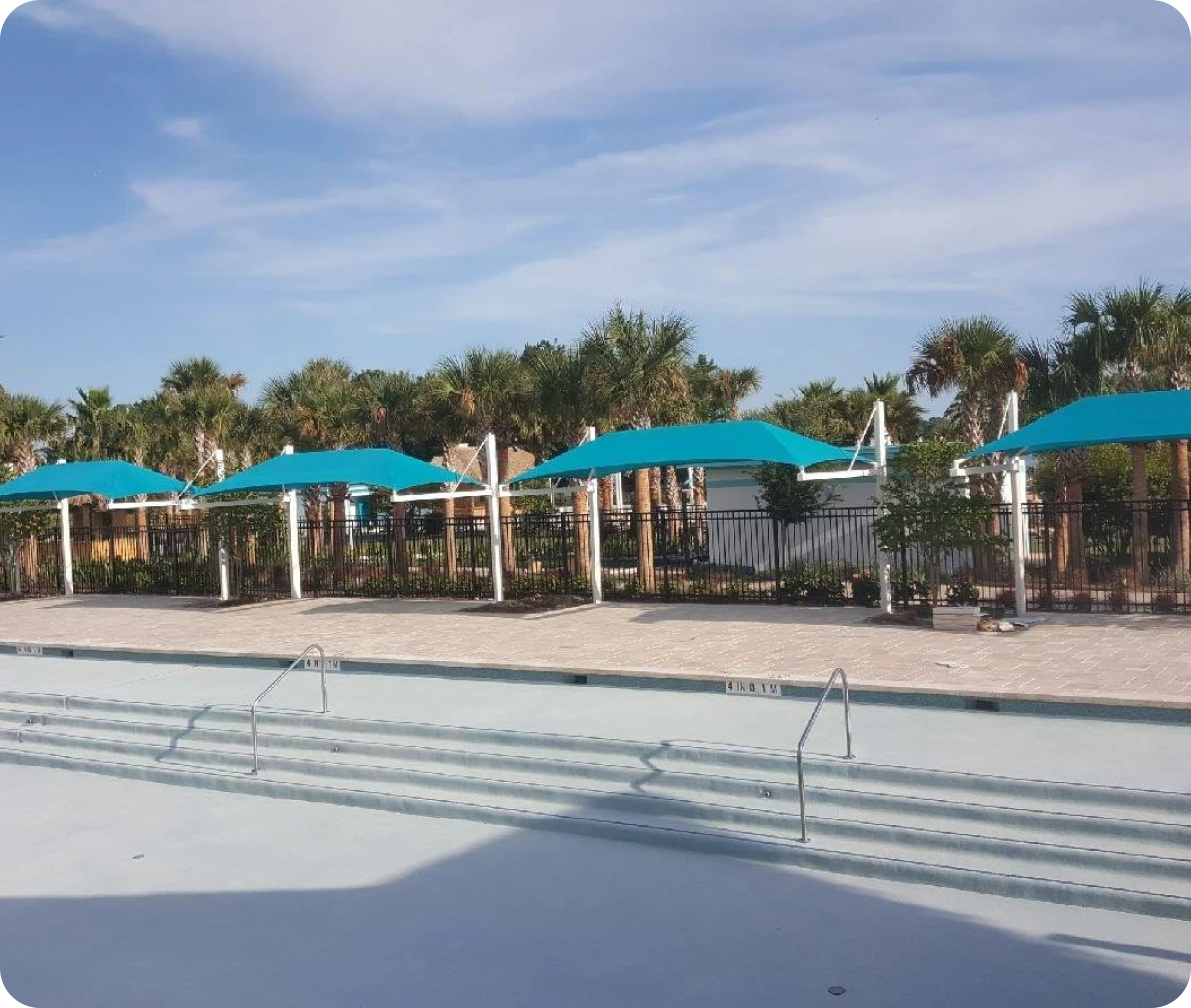 Empty pool with blue umbrellas and palm trees.