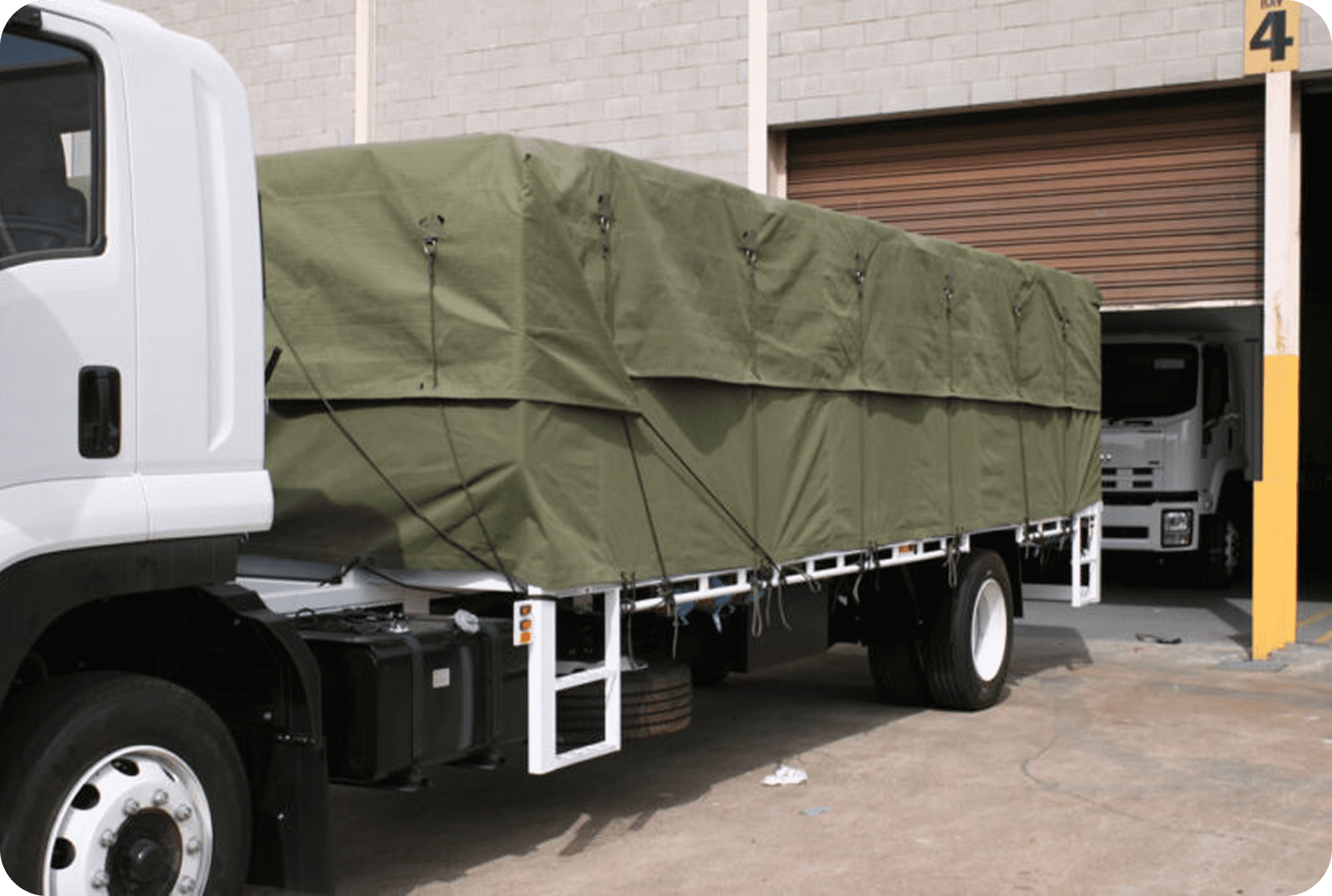Truck with green tarpaulin parked at warehouse.